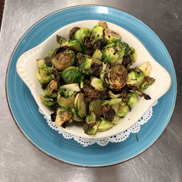 Roasted Brussels sprouts with balsamic glaze in a white bowl on a blue plate.