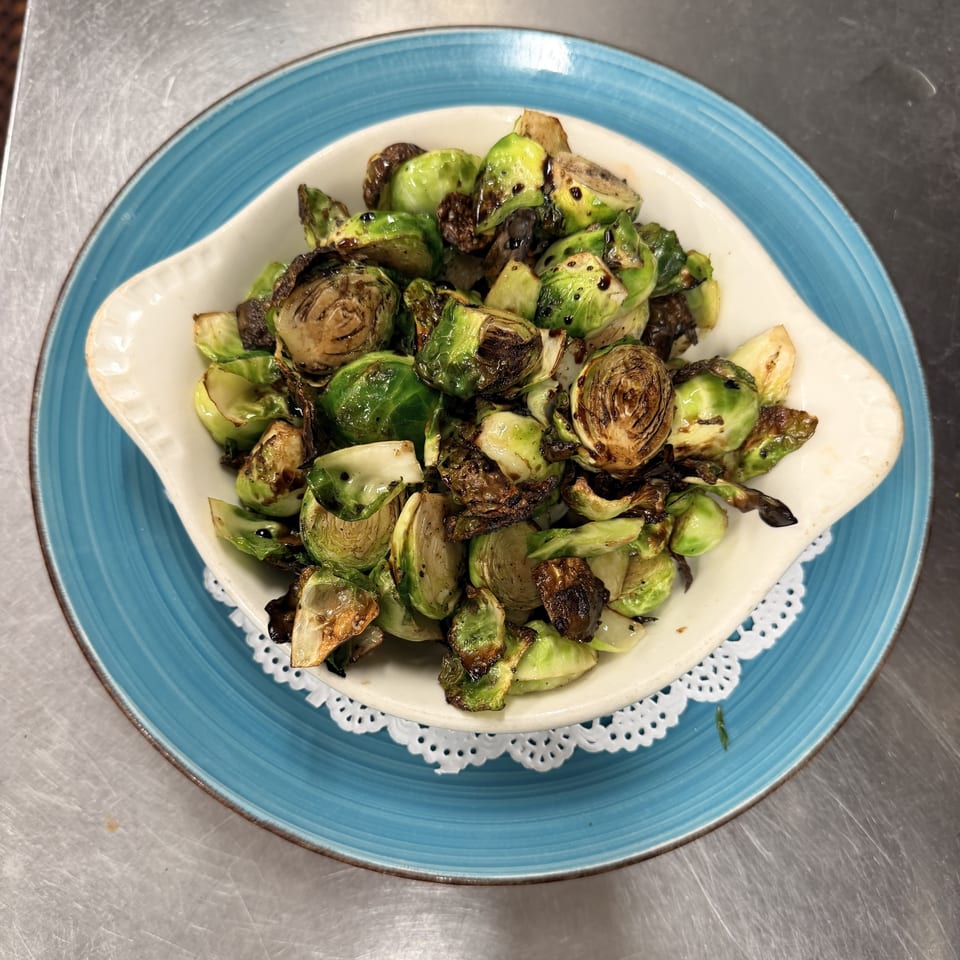 Roasted Brussels sprouts with balsamic glaze in a white bowl on a blue plate.