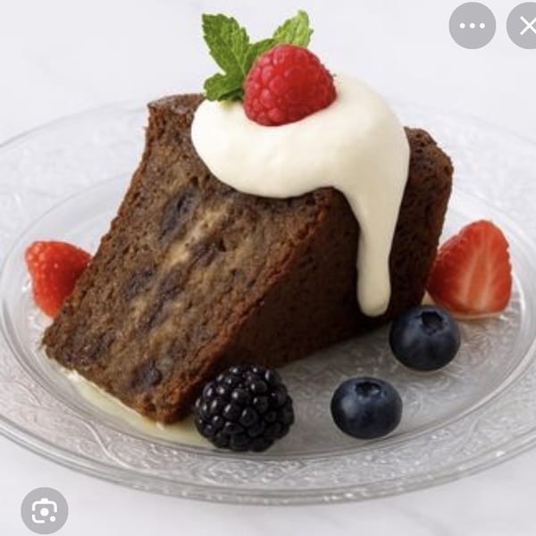 Dark cake slice topped with cream, raspberry, mint, and mixed berries on a clear plate.