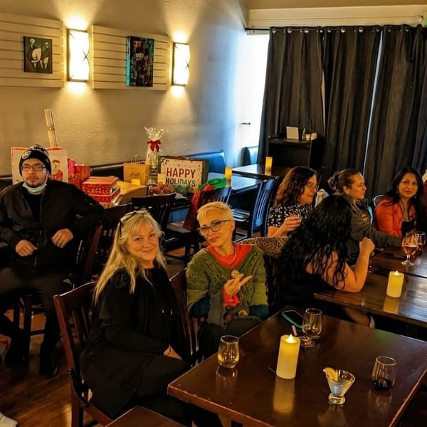 A group of people gathered at tables in a restaurant, celebrating with drinks and gifts.