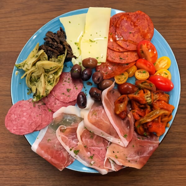 A vibrant charcuterie board with various meats, cheeses, olives, tomatoes, and marinated vegetables.