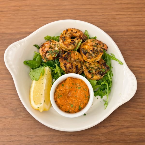 Grilled shrimp on a bed of arugula with a lemon wedge and a side of red sauce.