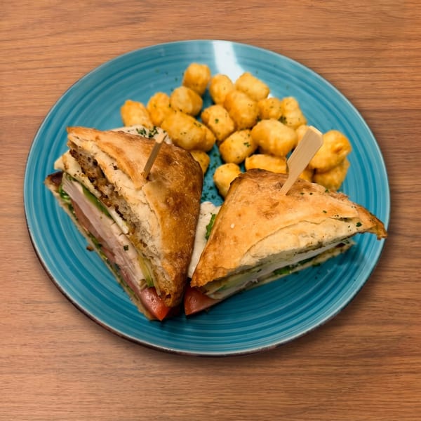 Two halves of a club sandwich with tater tots on a blue plate.