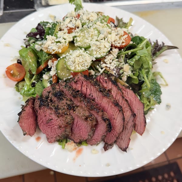Sliced medium-rare steak served with a fresh salad of greens, tomatoes, cucumbers, and blue cheese.
