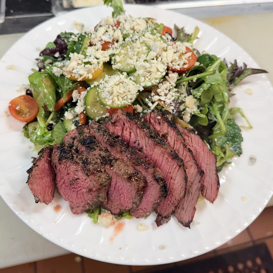 Sliced medium-rare steak served with a fresh salad of greens, tomatoes, cucumbers, and blue cheese.