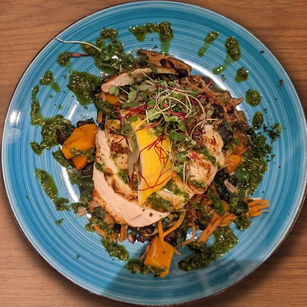 Grilled chicken with pesto, lemon, microgreens, and vegetables on a blue plate.