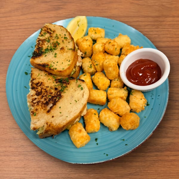 Grilled sandwich halves, tater tots, a lemon wedge, and ketchup on a blue plate.