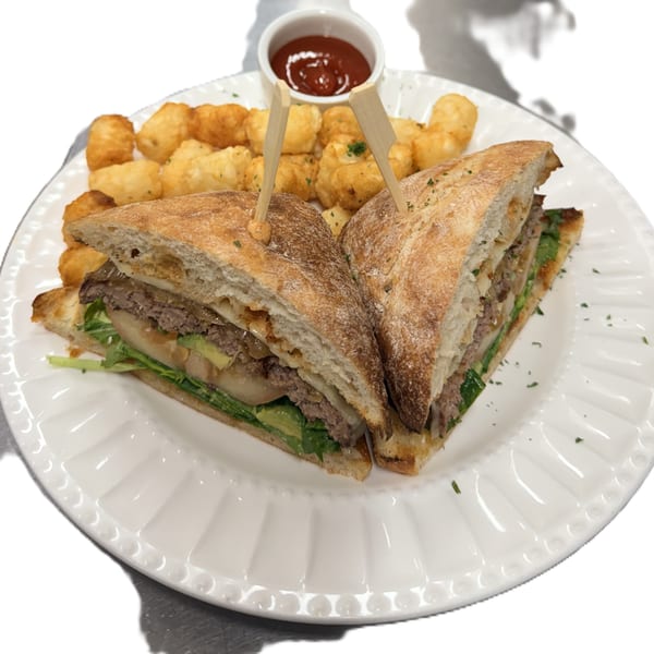 Hearty sandwich with beef, avocado, and caramelized onions, alongside crispy tater tots and ketchup.