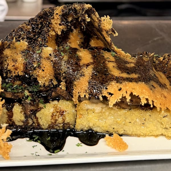 Savory polenta dish topped with mushrooms, a large cheese crisp, balsamic glaze, and a lemon wedge.