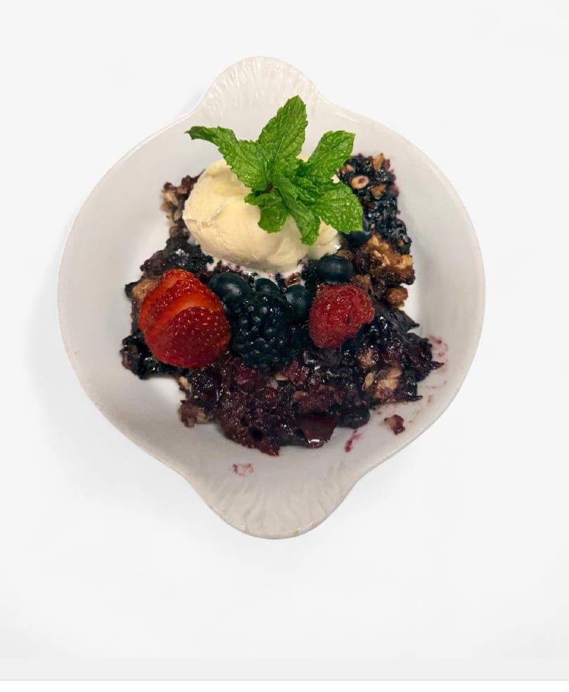 Berry crumble dessert topped with vanilla ice cream, fresh mint, strawberries, blueberries, and raspberries.