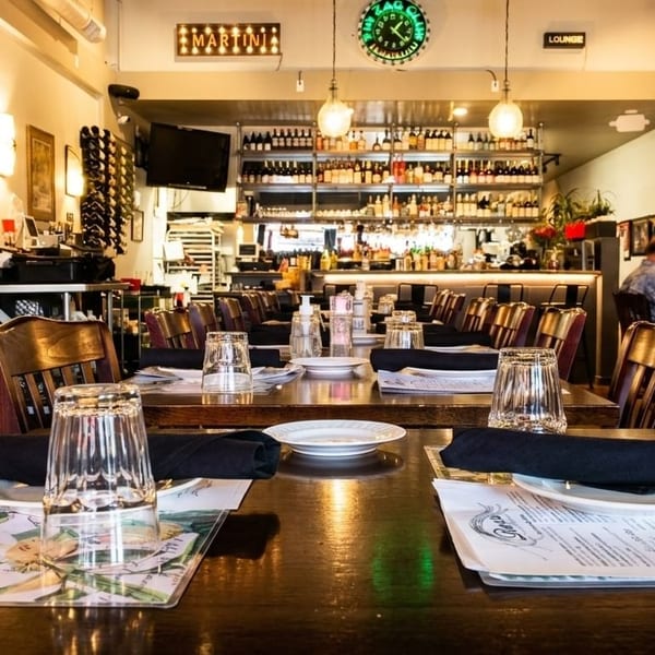 Restaurant interior with set tables, wooden chairs, a bar in the background, and a man dining.