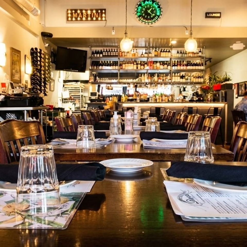 Restaurant interior with set tables, wooden chairs, a bar in the background, and a man dining.