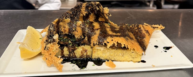 Polenta with mushrooms, balsamic glaze, and a parmesan crisp, garnished with a lemon wedge.