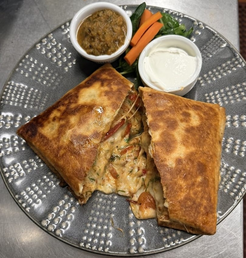 Golden-brown quesadilla, cut open to reveal melted cheese and vegetables, served with two dipping sauces.