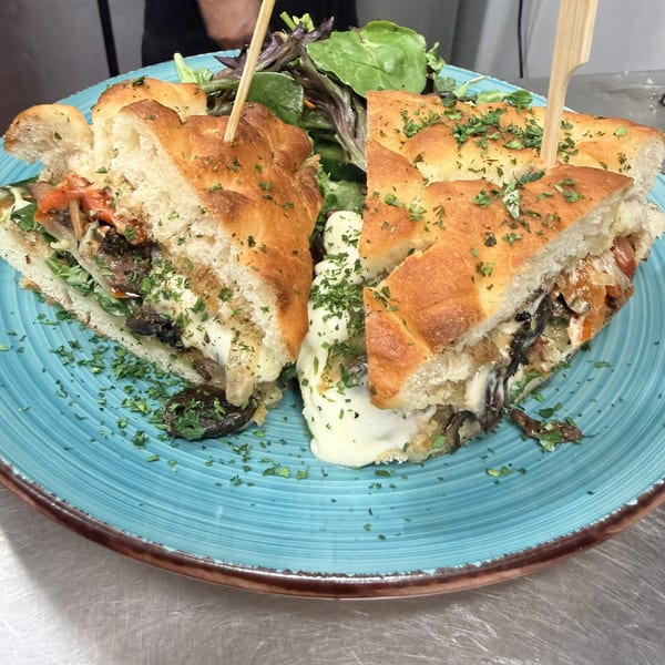 Focaccia sandwich with mushrooms, peppers, and melted cheese, garnished with parsley and a side salad.