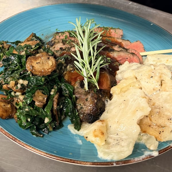 Sliced steak with rosemary, creamed potatoes, and sautéed greens with mushrooms on a blue plate.
