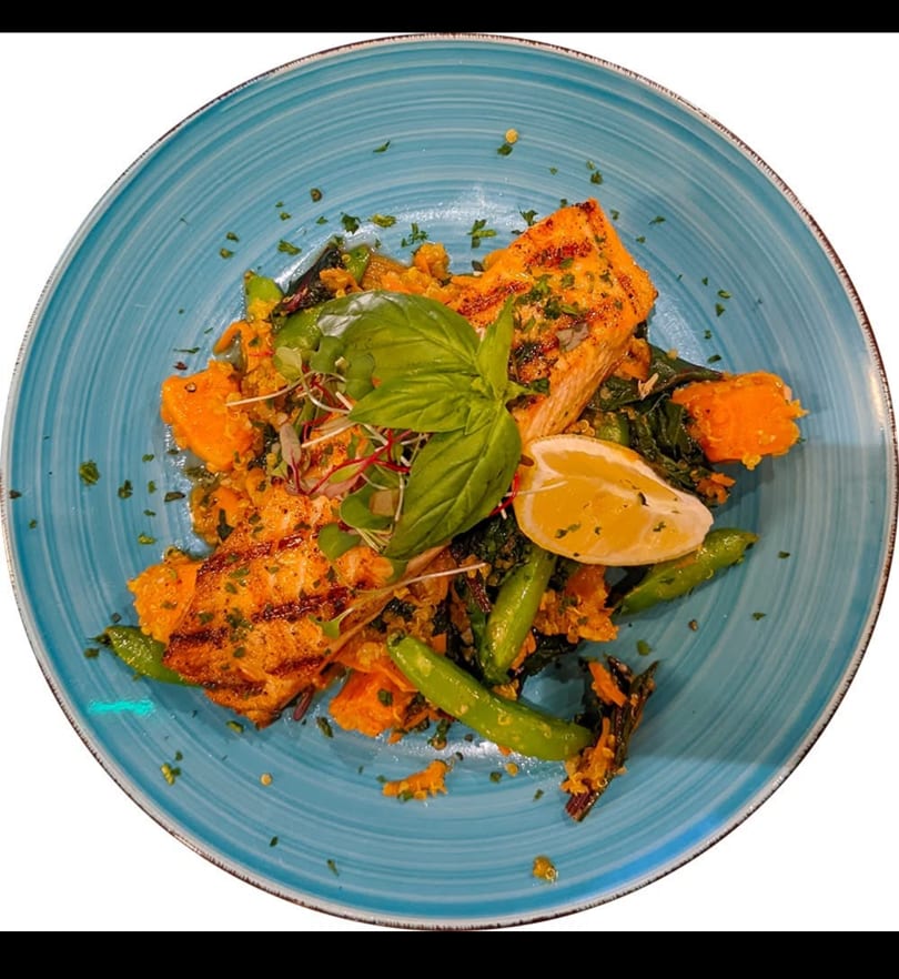 Grilled salmon with sweet potato, green beans, and a lemon wedge on a blue plate.