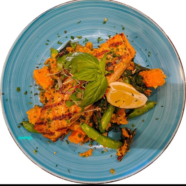 Grilled salmon with quinoa, sweet potato, green vegetables, lemon, and basil on a blue plate.