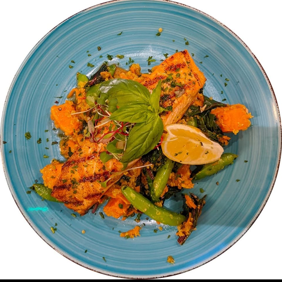 Grilled salmon with quinoa, sweet potato, green vegetables, lemon, and basil on a blue plate.
