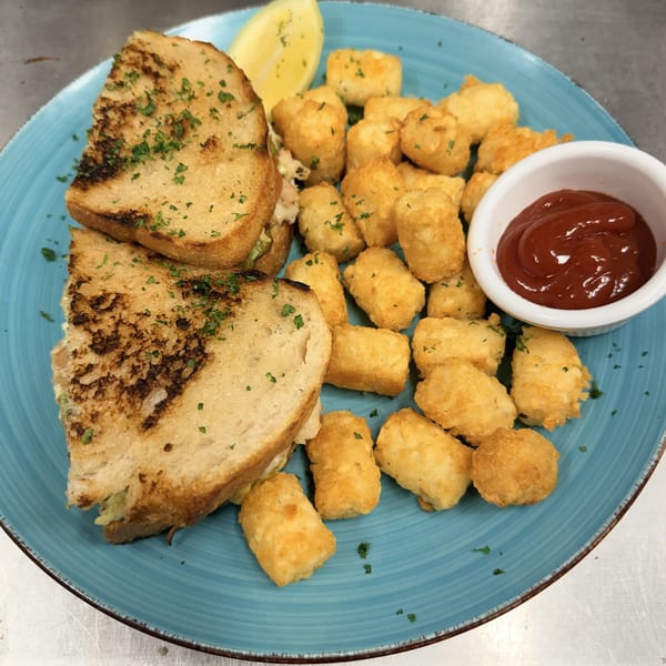 Grilled sandwich halves, golden tater tots, lemon wedge, and ketchup on a blue plate.