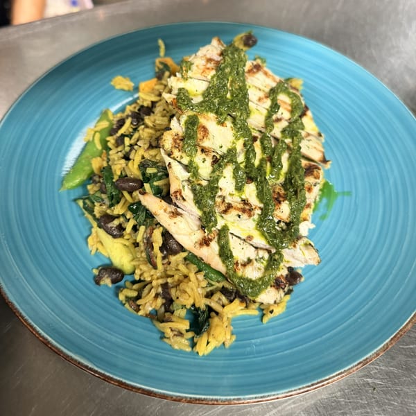 Grilled chicken with green sauce, orzo, black beans, and vegetables on a blue plate.