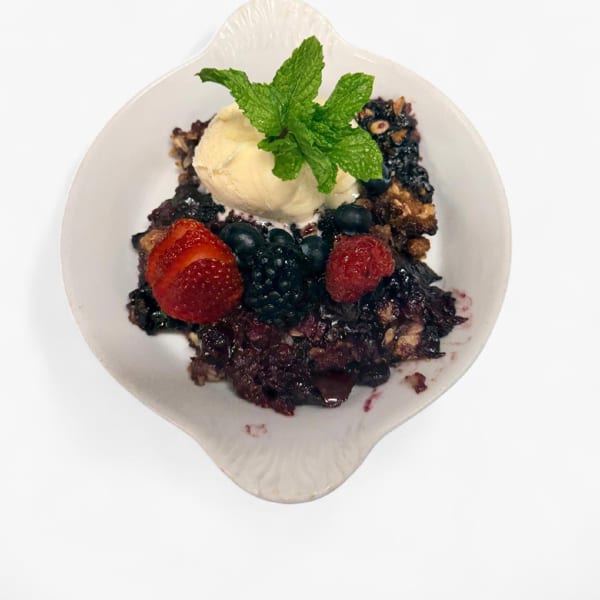 Berry crumble with vanilla ice cream, fresh berries, and mint in a white dish.