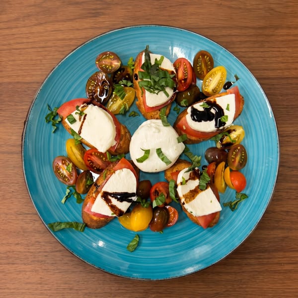 Caprese bruschetta with fresh mozzarella, tomatoes, basil, and balsamic glaze on a blue plate.