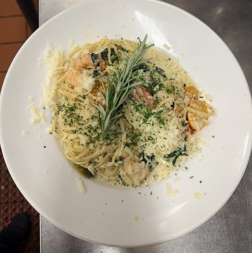Creamy pasta with shrimp, spinach, tomatoes, parmesan, parsley, and a rosemary sprig.