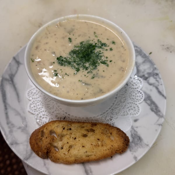Creamy soup topped with parsley, served with a slice of toasted bread on a marble plate.