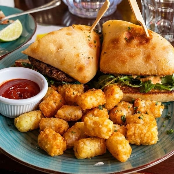 Two burgers with tater tots and ketchup on a blue plate, with an empty plate nearby.